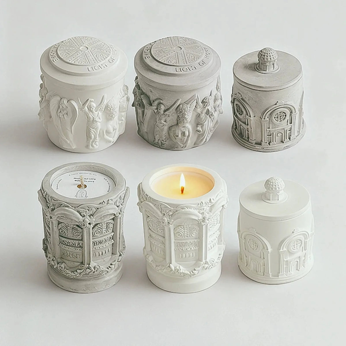 Six original relief candles showing three designs in white and gray finishes, with patterned lids and raised details.