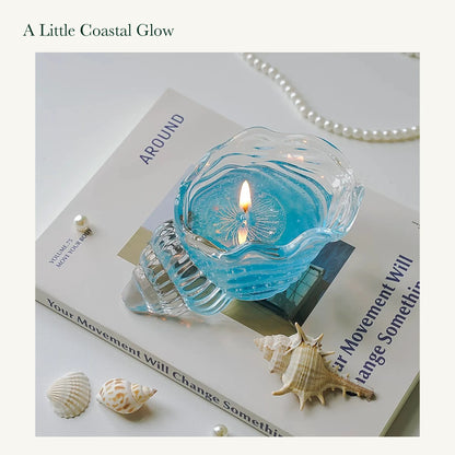 A lit blue conch-shaped glass candle on a book, showing its original glass ridges and patterned wax.