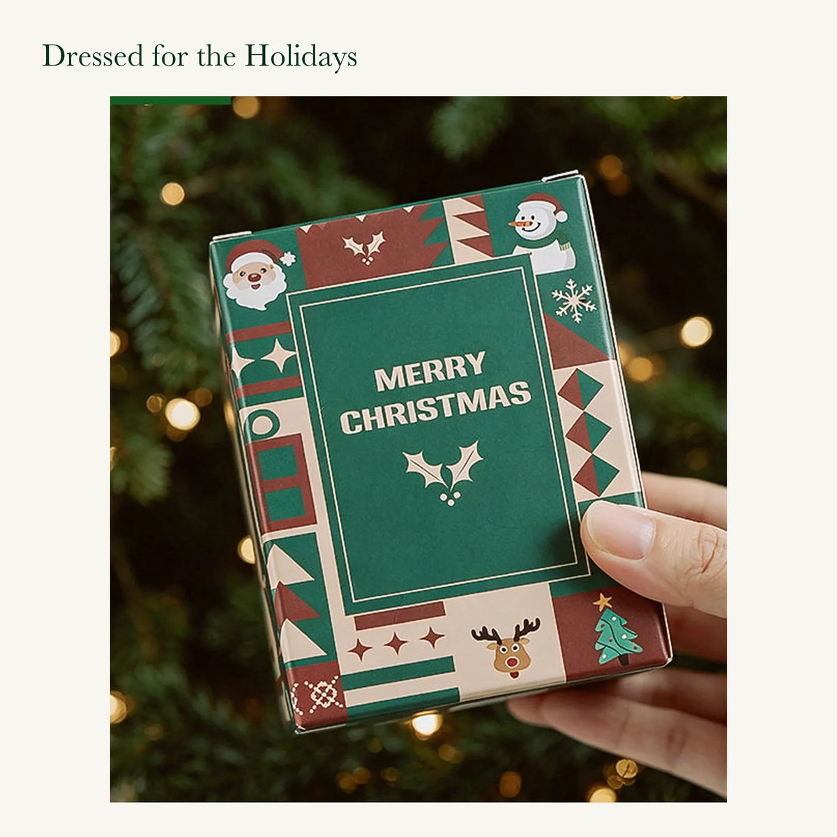 Hand holding the original green and red Merry Christmas candle box with its printed festive artwork.